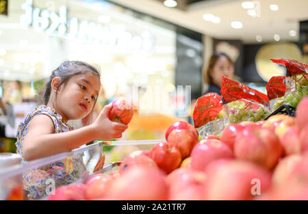 Asian bambina scegliendo un Apple in un negozio di alimentari o supermarket Foto Stock