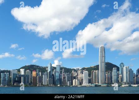 Un ampio angolo di vista del porto di Hong Kong e i grattacieli di Hong Kong Island sotto un cielo azzurro con soffici nuvole bianche Foto Stock
