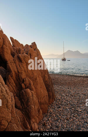Uno yacht, granito rosso formazioni rocciose e spiaggia di Plage de Ficaghjola / Plage de Ficajola e il golfo di Porto, Calanques de Piana Corsica Francia. Foto Stock