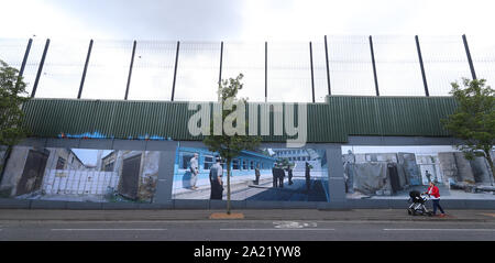 Una donna cammina passato a Belfast parete di pace che esibisce le foto dal fotografo tedesco Kai Wiedenhofer del mondo???s pareti di confine, precedendo Brexit. Foto Stock