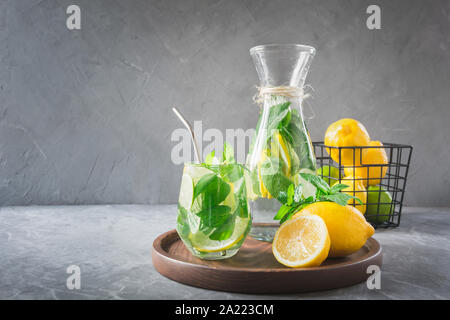 Detox acqua o limonata con succo di limone e menta, citrics in vetro su un tavolo di legno e il fondale grigio. Close up. Inquadratura orizzontale Foto Stock