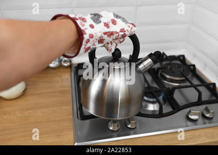 Man mano in muffole holding metalic bollitore in cucina Foto Stock
