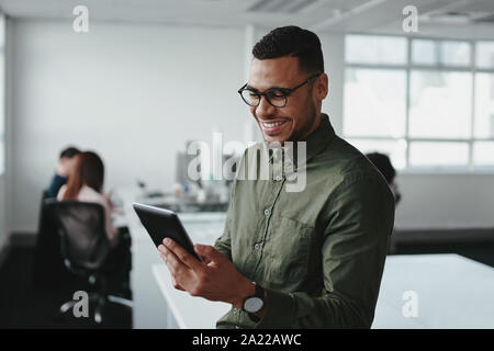 Sorridente giovane impreditore toccando lo smartphone e controllare online le informazioni in ufficio moderno Foto Stock