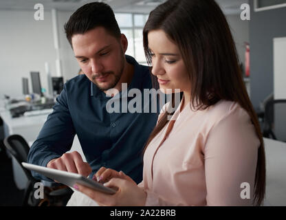 Close-up del giovane imprenditore che mostra i dati sulla tavoletta digitale schermo per imprenditrice sorridente in ufficio Foto Stock