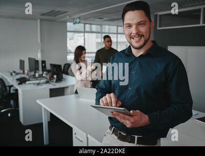 Ritratto di un fiducioso corporate executive utilizzando una tavoletta digitale in un ufficio moderno guardando la fotocamera Foto Stock