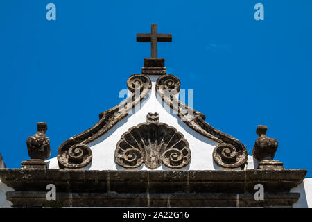 Triangolo del tetto di una chiesa con bordi ornati e una croce. Facciata bianca. Azzurro cielo. Ribeira Grande, Sao Miguel, isole Azzorre, Portogallo. Foto Stock