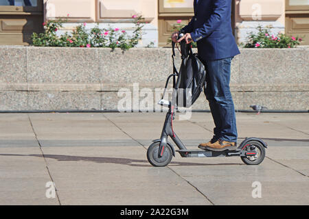 Uomo a cavallo di un kick scooter presso la piazza della città Foto Stock