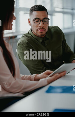 Close-up di una imprenditrice che mostra qualcosa sulla tavoletta digitale al suo collega di sesso maschile in office meeting Foto Stock