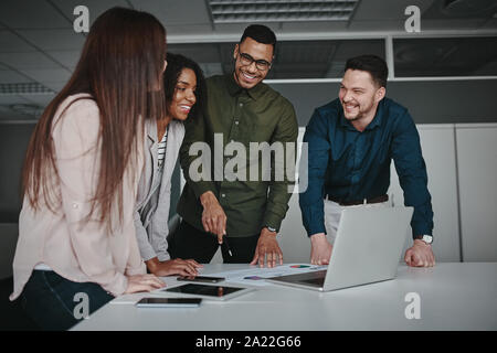 Gruppo di giovani multirazziale business persone in piedi insieme alla scrivania in ufficio per discutere la strategia aziendale guardando al laptop Foto Stock