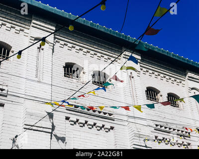 Colorati bandiere di partito di close-up di carta brillante bandiere, lampadine luci appesa sopra il profondo blu del cielo e antico edificio di pietra di sfondo festival città di concetto Foto Stock