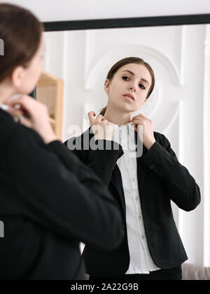 Ottenere lavoro di preparazione per il colloquio Ragazza in un abito di business è la raddrizzatura del collare della camicia di lei in piedi di fronte allo specchio Foto Stock