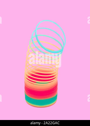 Multicolore in plastica slinky luminose molla a spirale giocattolo in posizione verticale su un sfondo rosa Foto Stock