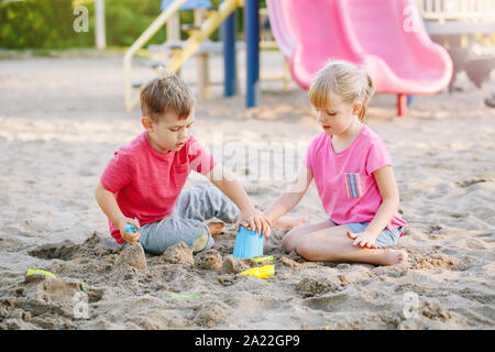 Bambini Un ragazzo e una ragazza amici giocare i bambini in età prescolare con sabbia e giocattoli in sandbox su giornata estiva all'esterno. Infanzia felice stile di vita. Autentica real pers Foto Stock