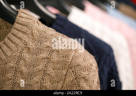 Vari cavo a maglia Maglioni o maglie su hanger rack in un negozio di abbigliamento o in un armadio, il fuoco selettivo Foto Stock