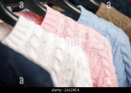 Vari cavo a maglia Maglioni o maglie su hanger rack in un negozio di abbigliamento o in un armadio, il fuoco selettivo Foto Stock