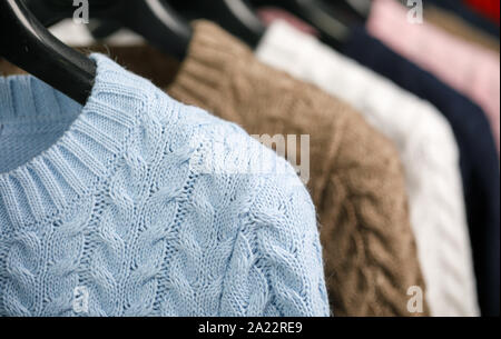 Vari cavo a maglia Maglioni o maglie su hanger rack in un negozio di abbigliamento o in un armadio, il fuoco selettivo Foto Stock