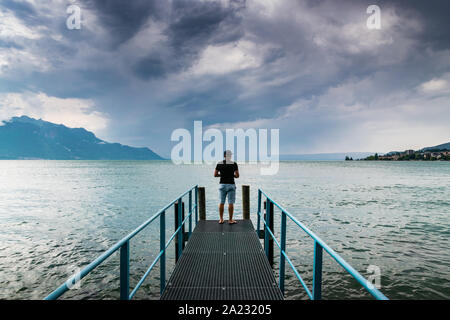 L uomo è in piedi su una piattaforma in acciaio presso il Lago di Ginevra a distanza le nuvole scure e pioggia,Montreux, Svizzera. Foto Stock