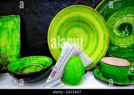 Un tovagliolo di flanella sullo sfondo di una collezione di bella mano di piatti in ceramica di varie capacità, ricoperta di verde brillante smalto. Foto Stock