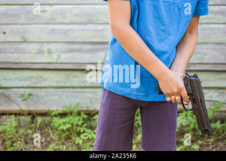 Ragazzo tiene nelle sue mani della pistola sullo sfondo di un vecchio di legno un muro esterno Foto Stock