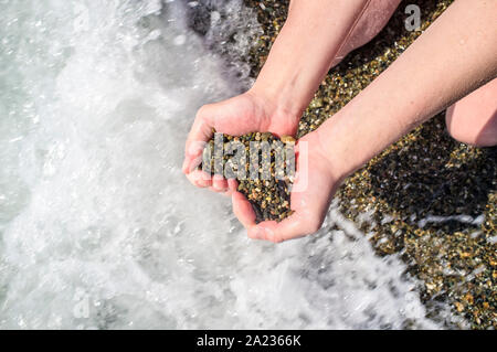 Il simbolo del cuore da pietre in una femmina di mano su uno sfondo del Mar Nero. Progettazione Concettuale. Foto Stock