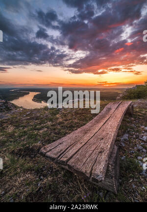 Bellissimo tramonto sul paesaggio con fiume Danubio. Panca in legno in primo piano. Foto Stock