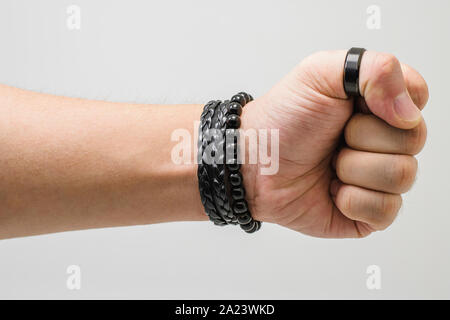 Punch mano. La mano di un uomo bianco vestita di nero gli accessori con un pugno chiuso dando un punzone. Bottom-up visualizza, sfondo bianco. Foto Stock