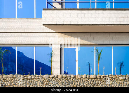 Bella riflessione di sky sulla coperta di pannelli di vetro di un edificio circondato da una recinzione di pietra. Da Muscat Oman. Foto Stock