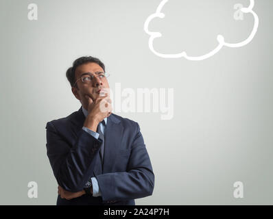 Imprenditore in abiti formali e occhiali pensare profondamente alla ricerca di distanza con una mano sul mento Foto Stock