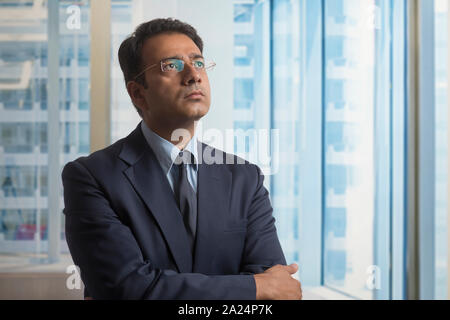 Imprenditore in abiti formali e occhiali pensare profondamente alla ricerca di distanza con le braccia incrociate Foto Stock