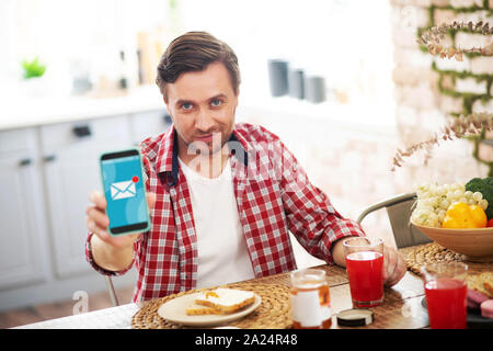 Dai capelli scuri azienda uomo smartphone durante la lettura di messaggi di posta elettronica Foto Stock