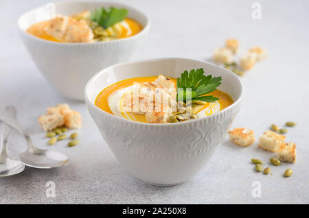 Zuppa di zucca con panna, crostini, semi di zucca e prezzemolo sul grigio di un calcestruzzo o pietra dello sfondo. Foto Stock