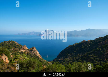 Le montagne e il mare paesaggio con una solitaria ormeggiati yacht a vela nel Golfo di Porto visto dalla piana nella parte occidentale della Corsica Mediterraneo. Foto Stock