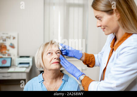 Medico donna gocciolamento di gocce per gli occhi sugli occhi di un senior paziente durante un trattamento presso l'ufficio oftalmologica Foto Stock