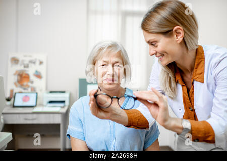 Oculista offrendo occhiali per visione a un senior donna paziente durante una consultazione medica in ufficio Foto Stock