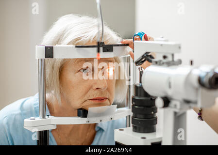 Senior donna durante un medico di occhio esame con microscopio in ufficio oftalmologici Foto Stock