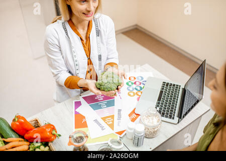 Nutrizionista azienda broccoli freschi, lavorando a un programma di dieta in ufficio Foto Stock