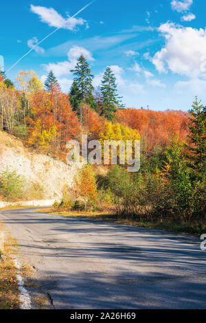 Strada di campagna attraverso il bosco in montagna. trasporto bellissimo paesaggio autunnale mattinata. alberi a foglie colorate. Il vecchio asfalto screpolato surfa Foto Stock