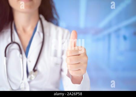 Bel giovane medico donna che indossa uno stetoscopio su sfondo ospedale approvazione facendo gesto positivo con la mano, pollice in alto sorridente e felice per s Foto Stock