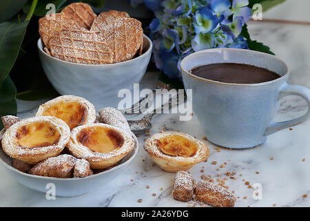 Pasta sfoglia e crema inglese dolci accompagnati da una tazza di cioccolato. Marmo bianco sullo sfondo blu e fiori. Foto Stock