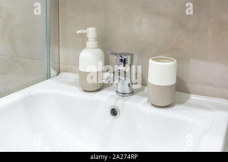 Il sapone e lo shampoo dispenser vicino ceramica rubinetto acqua lavandino con rubinetto in costosi loft bagno Foto Stock