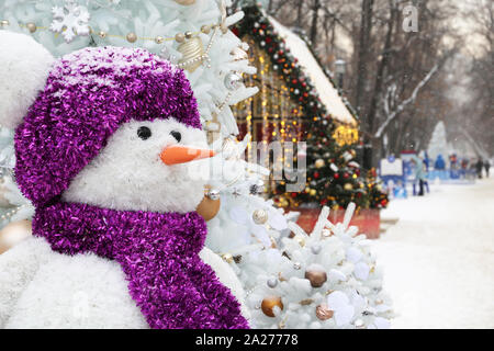 Pupazzo di neve su una strada in inverno, le decorazioni di Natale in città. Nuovo anno celebrazione durante la nevicata Foto Stock