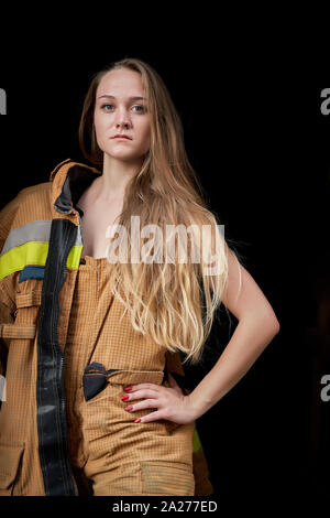 Immagine della giovane donna pompiere in tuta nera su sfondo vuoto in studio Foto Stock