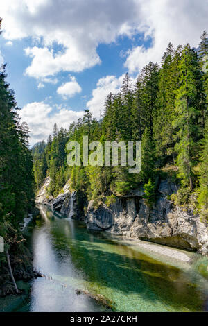 Vista verticale di un paesaggio idilliaco con un lago di montagna e una piccola cascata circondata dal verde della pineta Foto Stock