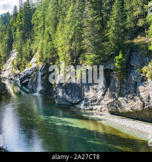 Formato quadrato vista di un paesaggio idilliaco con un lago di montagna e una piccola cascata circondata dal verde della pineta Foto Stock