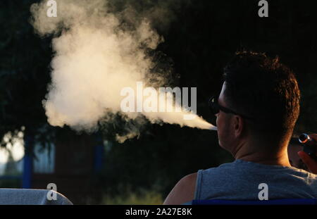 L'uomo soffiando grande nube di fumo da vaping Foto Stock