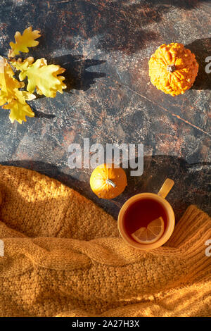 Autumntime laici piatta con maglione giallo, zucche decorative, foglie di autunno e la tazza di tè nero con il limone su sfondo scuro Foto Stock
