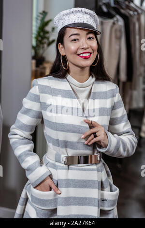 Allegro giovane donna indossa rivestimento a strisce nel negozio di moda Foto Stock