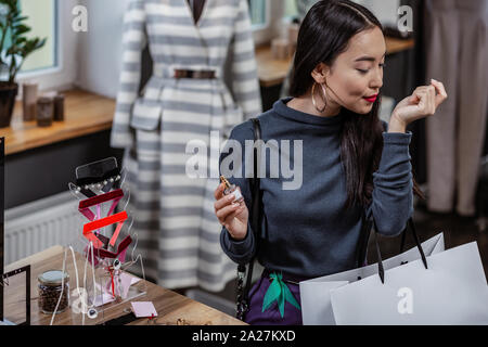Bella giovane donna test di un profumo sul suo polso in negozio Foto Stock