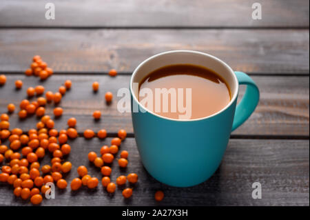 Una sana bacche di olivello spinoso succo in una tazza di colore blu su una tavola di legno. Le bacche sono nelle vicinanze. Stile rustico. Foto Stock