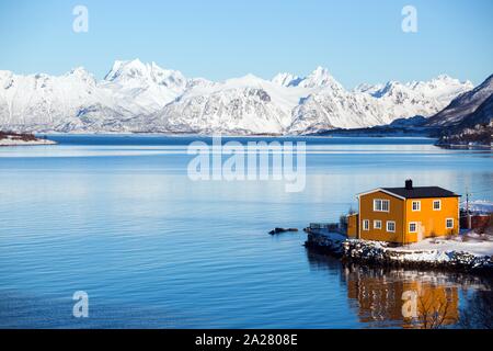 Tradizionale giallo norvegese casa in legno per stand presso il lago e le montagne in distanza. Isole Lofoten. La Norvegia. Foto Stock